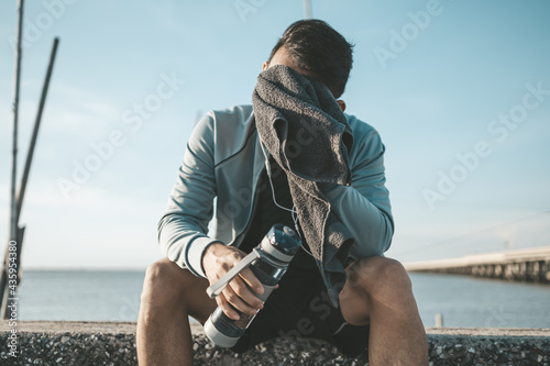sport man resting after a running and wipe the sweat by towel and hand hold water bottle. sport and workout concept.