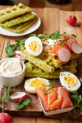 Spinach waffles with salmon, egg and radish. Side view, wooden background.