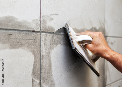 Grouting ceramic tiles. Tilers filling the space between tiles using a rubber trowel 