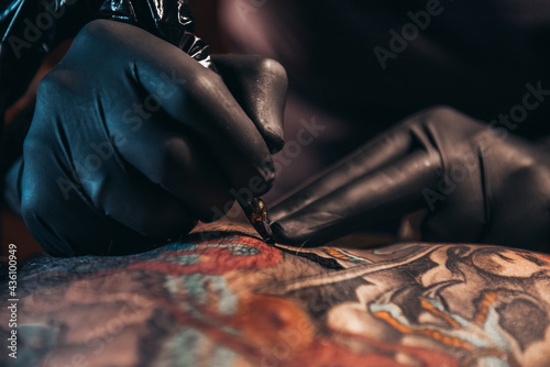 Hands of a tattoo artist wearing black gloves and holding a machine