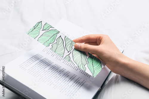 Woman with cute bookmark and book on bed