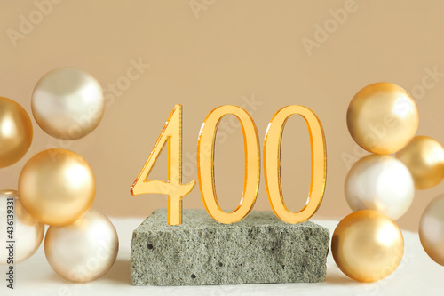 Number 400 on a concrete podium and volumetric golden balls on a beige background. Copy space..