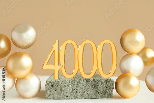 Number 4000 on a concrete podium and volumetric golden balls on a beige background. Copy space..