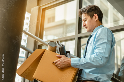 Businessman is carrying a brown cardboard box to resignation