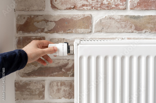 Woman adjusting thermostat of white radiator at home