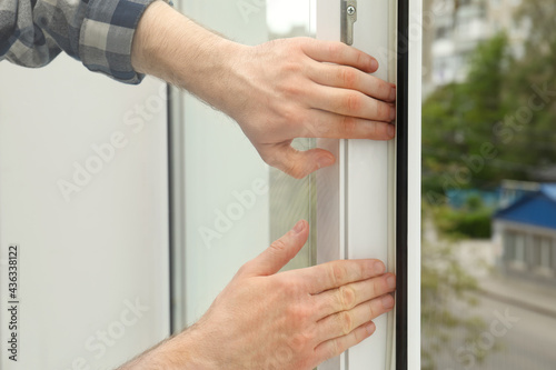 Worker putting rubber draught strip onto window indoors, closeup