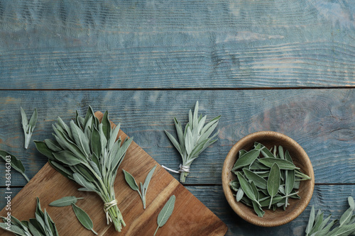 Fresh green sage with board and bowl on light blue wooden table, flat lay. Space for text