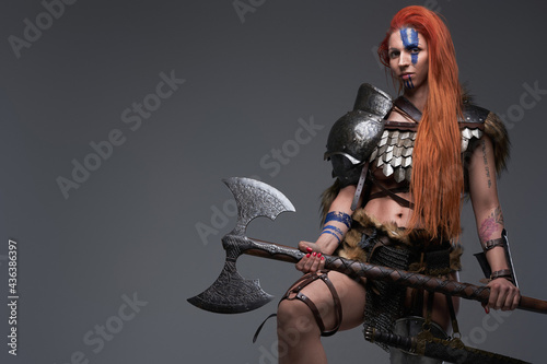 Brave and powerful woman viking with axe posing in gray background