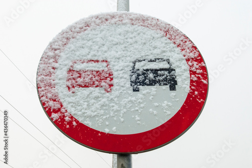 Znak zakazu wyprzedzania pojazdów w warunkach zimowych, pokryty śniegiem