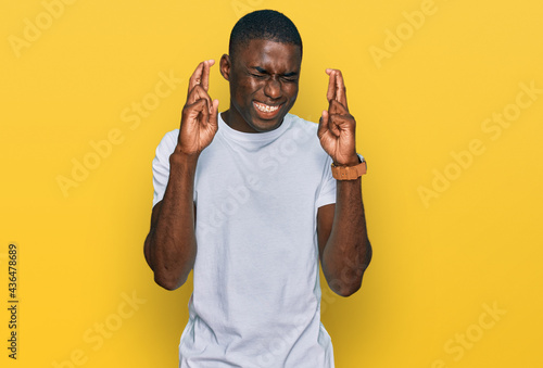 Young african american man wearing casual white t shirt gesturing finger crossed smiling with hope and eyes closed. luck and superstitious concept.