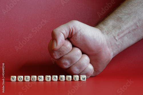 The inscription voluntarism and a clenched fist on a red background. The concept of voluntaristic oppression, coercion and lack of freedom