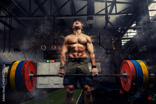 Weightlifter in the gym, visual effects of positive energy on training. Strong attractive man holds a heavy barbell in his hands and lifts a weight in a modern gym concept. Screaming during exercises