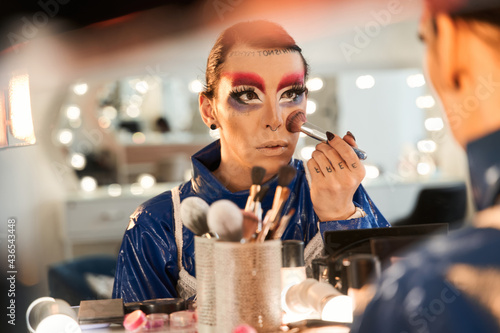 Drag queen looking at the mirror and applying blushes at his face