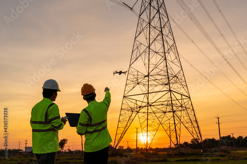 Team work of Engineers location help Technician use drone to flying inspect equipment instead of workers at the high voltage electric transmission tower, electric power station