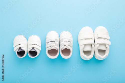 New white sport shoes on light blue table background. Pastel color. Closeup. Different sizes. Concept of child growing. Top down view.