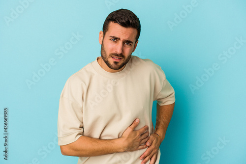 Young caucasian man isolated on blue background having a liver pain, stomach ache.
