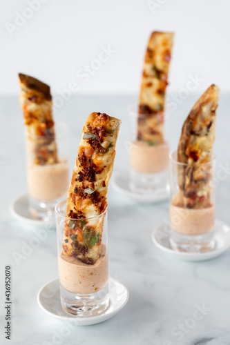 Four flatbread pizza stick appetizers in shot glasses with dip, against a light background.