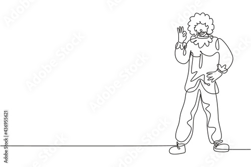 Single continuous line drawing clown stands with gesture okay wearing wig and clown costume ready to entertain the audience in circus arena. Dynamic one line draw graphic design vector illustration