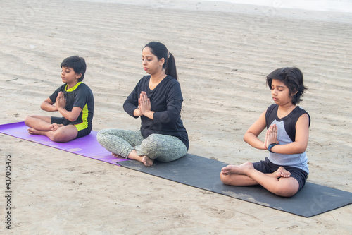 Woman with two boys meditating at beach