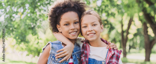 Two little girls hugging in the park. Diverse multi ethnic kids friends playing together outdoor. Summer fun, friendship, diversity, vacations concept