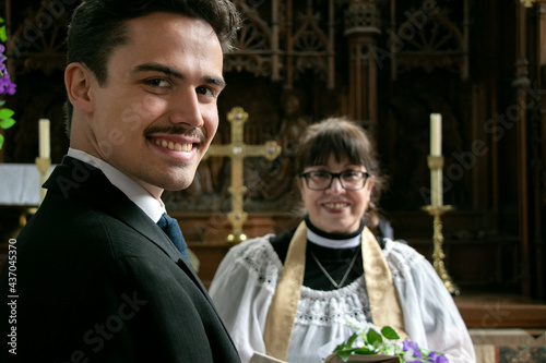 Gay groom waits for his husband at altar in church with vicar in the background