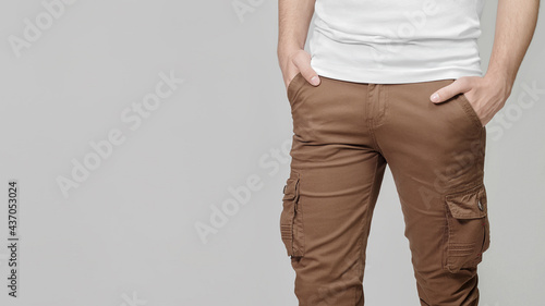 Model wearing brown cargo pants with hands in pockets on grey background, empty place for text on the left. Mockup, template.