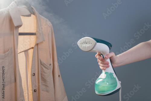 female hand with steamer and shirt on blue background