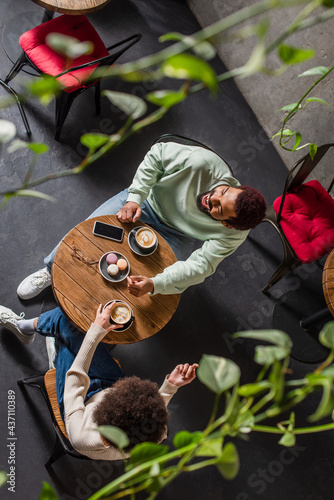 Overhead view of cheerful african american man sitting near girlfriend, coffee and cellphone in cafe