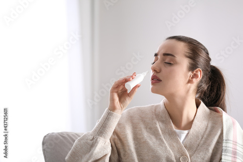 Sick young woman using nasal spray at home