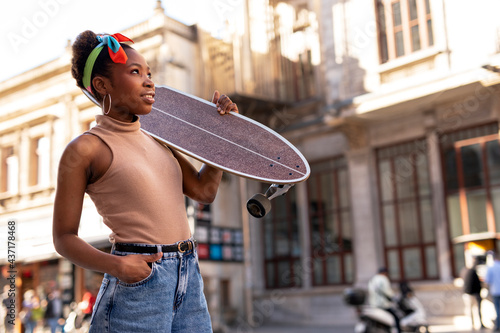 Portrait of happy african-american woman with skateboard. Young stylish woman with skateboard outdoors..