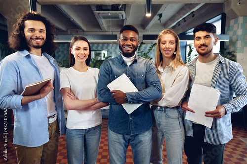 Group portrait of five diverse young colleagues standing in a row in office