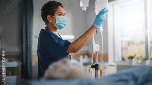 Hospital Ward: Professional Black Head Nurse Wearing Face Mask Does Checkup of Patient's Vitals, Checking Heart Rate Computer, Intravenous or Iv Fluids Drip Bag. Caring Nurse Monitors Person Recovery