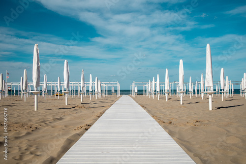 Riviera Romagnola spring view. Almost summer, clue skies, white walking path, sunbeds and umbrellas ready for season opening. Italian vintage riviera beach on the adriatic coast. 
