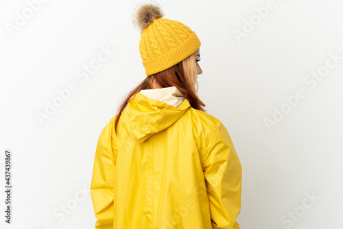 Teenager blonde girl wearing a rainproof coat over isolated white background in back position and looking side