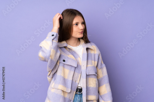 Teenager caucasian girl isolated on purple background having doubts while scratching head
