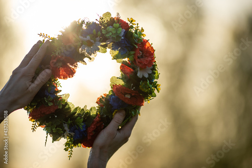 Hands with a wreath of Midsummer flowers against the sunset. Old Latvian culture tradition LIGO. Midsummer night celebrating in Latvia.