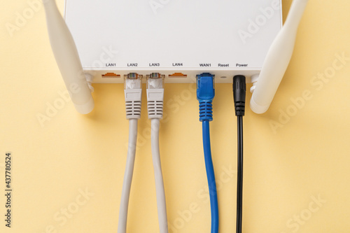White Wi-Fi wireless router with connected network and power cables on a yellow background. Home and office wlan router with inserted internet cables. Internet hardware close-up.