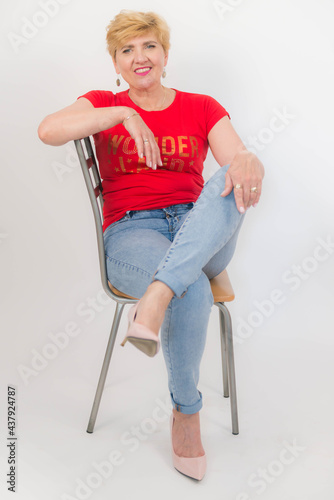 Zadbana, ładna, elegancka kobieta w średnim wieku ubrana w czerwoną bluzkę z krótkim rękawem, dżinsy i buty z obcasem.