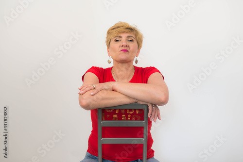 Zadbana, ładna, elegancka kobieta w średnim wieku ubrana w czerwoną bluzkę z krótkim rękawem, dżinsy i buty z obcasem.