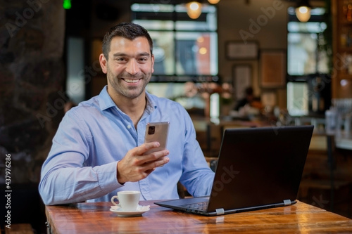 Hombre enviando un mensaje con el movil y su notebook laptop en un cafe despues del trabajo