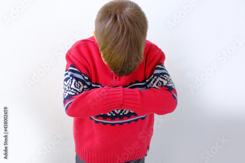 offended or punished child, a boy of 7-8 years old in a red Scandinavian sweater bent down on his face, hunched his back, parenting concept