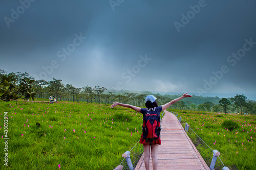 A beautiful woman with backpack happy on a field of Krachiew flowers and cloudy sky.