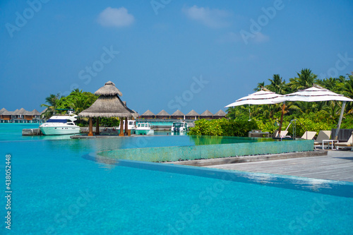 Scenic landscape of Maldives beach and pier with speed boats and yachts on the horizon. Seascape with water bungalows, beautiful turquoise sea and lagoon waters, tropical nature paradise. 