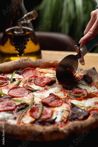 Close up of cutting a hot fresh pizza with a wheel knife, one hand is visible