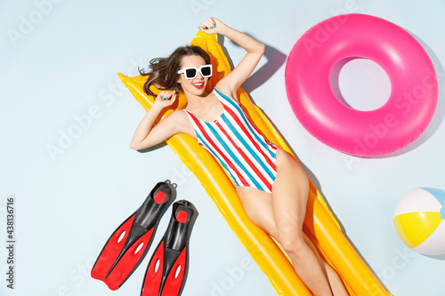 Top view young sexy woman slim body wear striped one-piece swimsuit lies on inflatable mattress ring ball hotel pool isolated on pastel blue color background. Summer vacation sea rest sun tan concept.