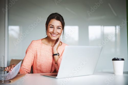 Young attractive female business analyst in pink jacket working at the laptop in cozy luxury office interior