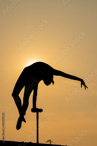 Flexible female circus Artist keep balance and touching the sun against dramatic sunset. Motivation, passion and achievement concept 