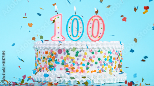 Colorful tasty birthday cake with candles shaped like the number 100. Pastel blue background.