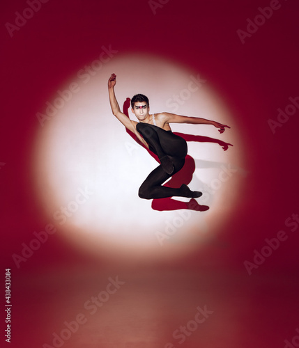 Ballet dancer dancing over red studio background. Modern design. Contemporary colorful conceptual light as rising sun at Japan.