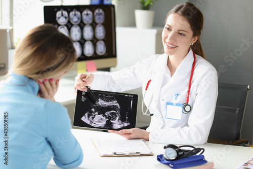Woman obstetrician gynecologist showing patient photograph of ultrasound examination of fetus on digital tablet